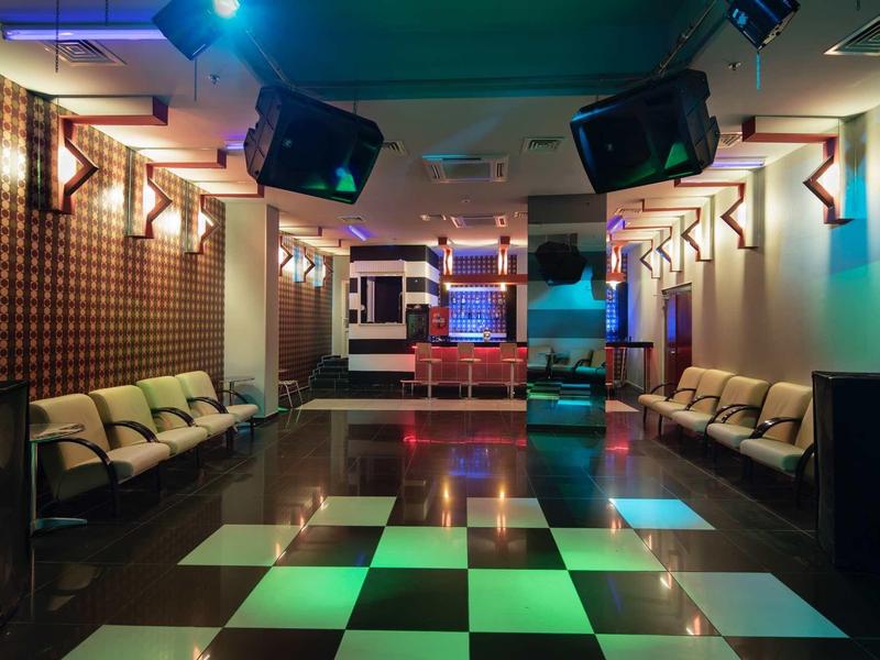 Moderní klubová místnost s šachovnicovou taneční podlahou a sezením podél stěn.