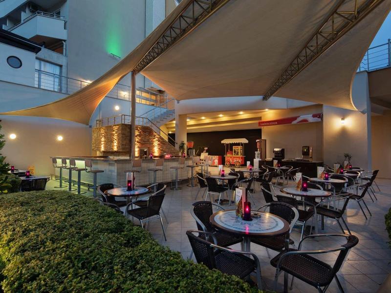 Příjemná venkovní část restaurace s stoly a židlemi pod velkou sluneční clonou.