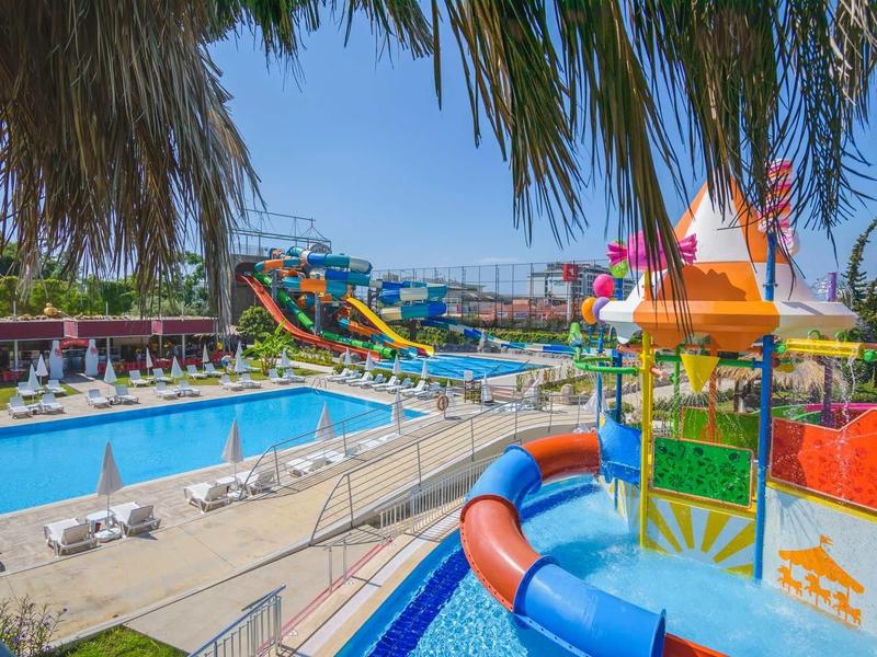 Barevný vodní park s bazény, skluzavkami a slunečníky pod palmami na dovolené.