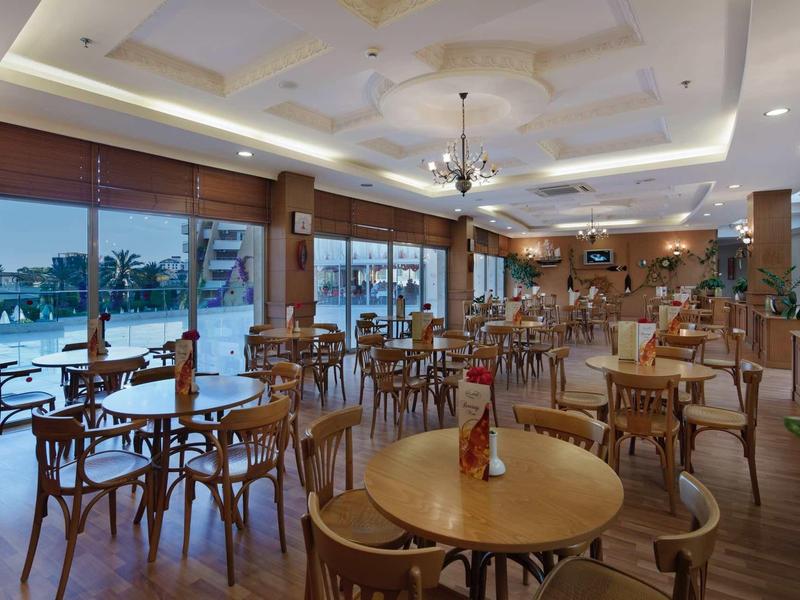 Světle osvětlená hotelová restaurace s dřevěnými židlemi a výhledem na bazén přes skleněná okna.