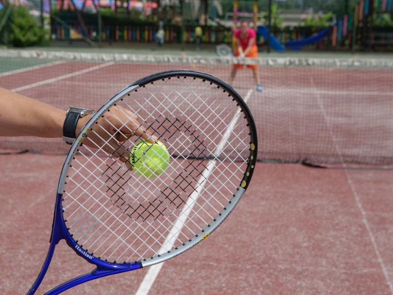 Hráč drží tenisovou raketu s míčkem na venkovním kurtu.