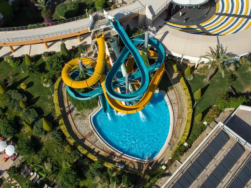 Letecký pohled na venkovní bazénovou oblast s velkými barevnými tobogány nad bazénem.