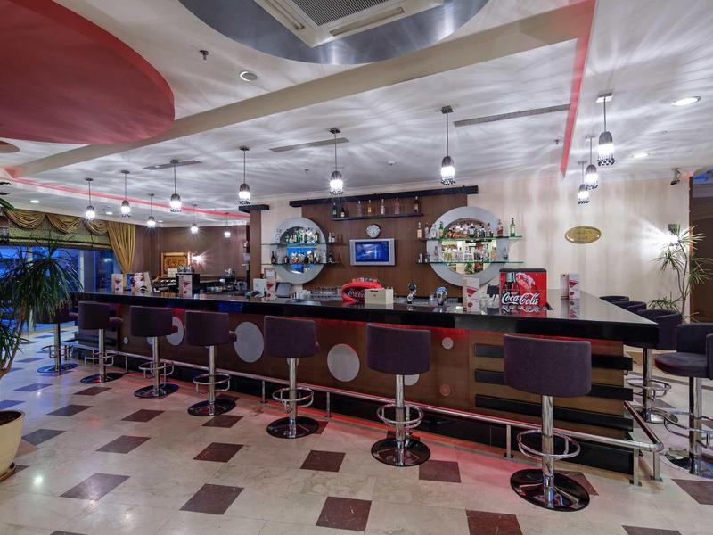 Moderní hotelový bar s elegantními stoličkami a kruhovým stropem v světlém prostředí.