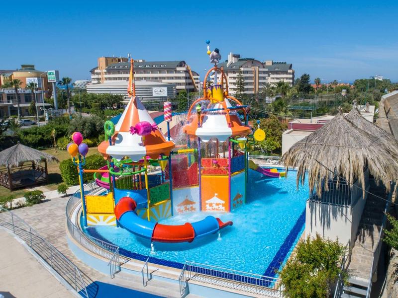 Barevné vodní hřiště s skluzavkami v bazénu před hotelovými budovami za slunečného dne