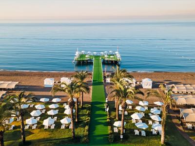 Blick auf Strand mit Liegen, Sonnenschirmen, Palmen und einem Steg im ruhigen blauen Meer.