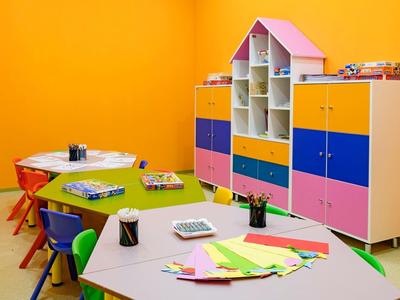 Buntes Klassenzimmer mit blau-gelben Regalen, bunten Stühlen und Tischen voller Bastelmaterial.