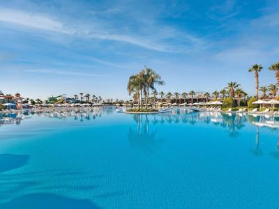 Grande piscina con palme e lettini sotto un cielo azzurro limpido