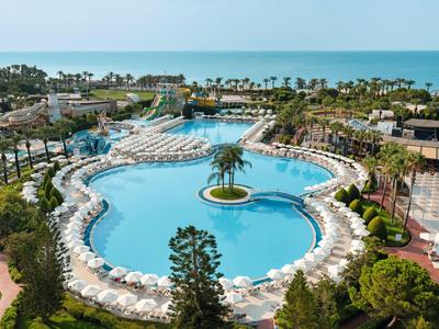 Großer, türkisfarbener Hotelpool mit Insel, weißem Sonnenschirmen und Palmen, am Meer gelegen.