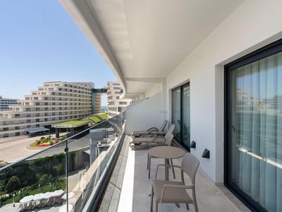 Balcony with chairs and tables overlooking modern hotel buildings and blue sky.