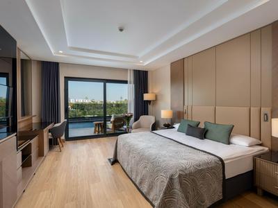 Modern hotel room with large bed, seating area, and balcony overlooking water.