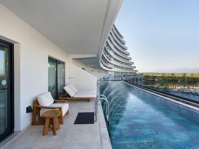 Modern hotel balcony with wooden chairs beside a long infinity pool overlooking a valley.