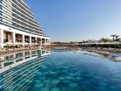 Large hotel pool with clear blue water and sun umbrellas in a modern hotel complex.