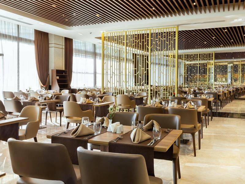 Interior elegante de restaurante con sillas marrones, mesas de madera y grandes ventanas con cortinas.
