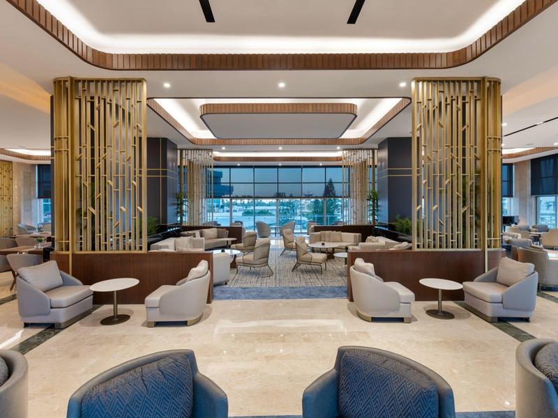 Restaurante de hotel moderno y luminoso con cómodos sillones y separadores dorados en diseño elegante.