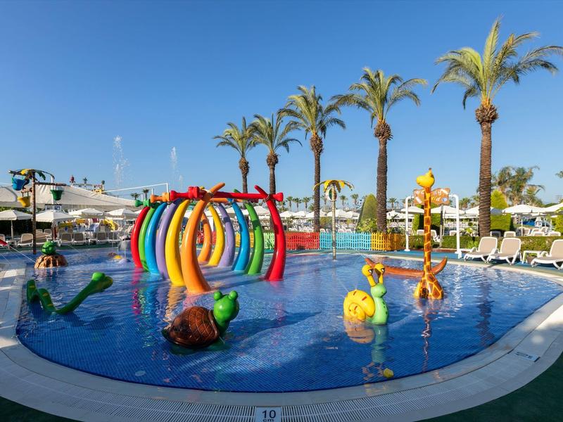 Piscina exterior colorida con parque acuático y palmeras bajo un cielo despejado en un resort vacacional.