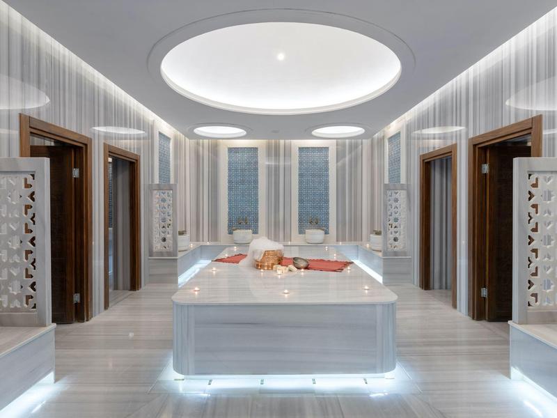 Área de spa moderna con mesa de masaje central, iluminación indirecta y cómodas camillas junto a la ventana.