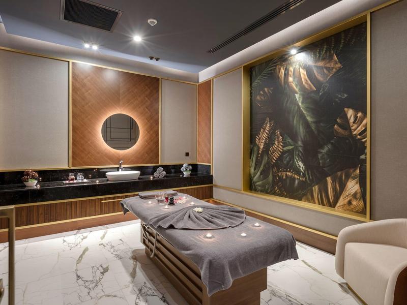 Sala de bienestar elegante con camilla de masaje, gran obra de arte y espejo redondo en la pared.