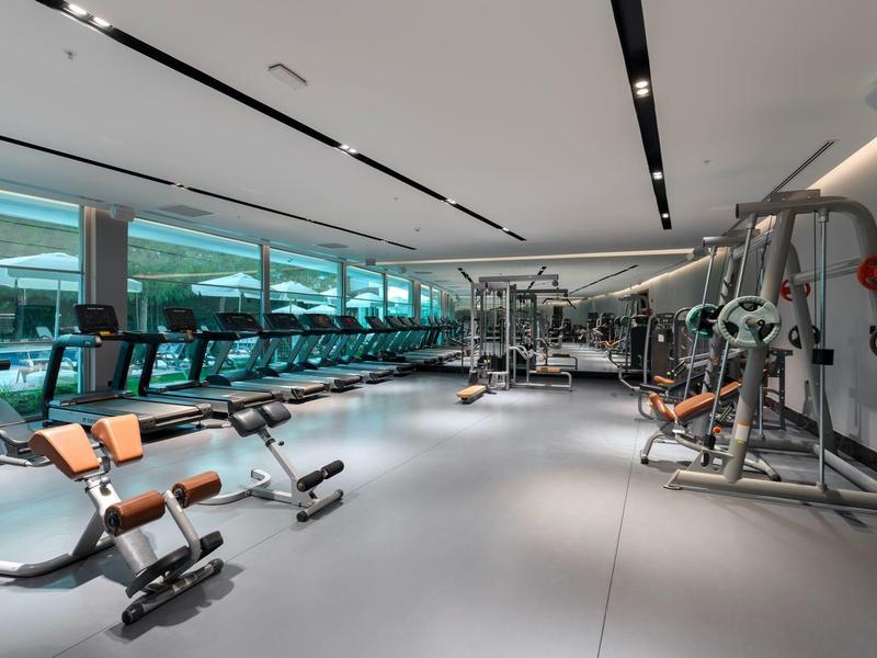 Gimnasio moderno de hotel con máquinas y grandes ventanas, área de entrenamiento luminosa y limpia.