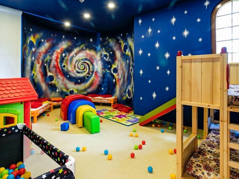 Sala de juegos infantil colorida con tobogán, estructura para trepar y pelotas de colores frente a un mural espiral.