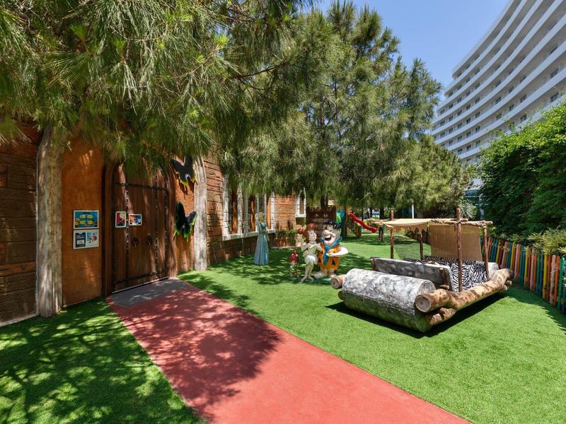 Un parque infantil con toboganes y áreas para sentarse junto a un camino rojo y áreas verdes en un hotel.