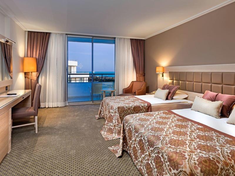 Habitación de hotel elegante con dos camas dobles, escritorio y balcón con vistas al mar al anochecer.