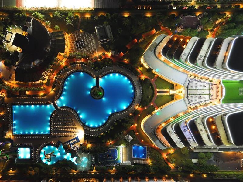 Foto nocturno de un hotel iluminado con varias piscinas de diferentes formas.