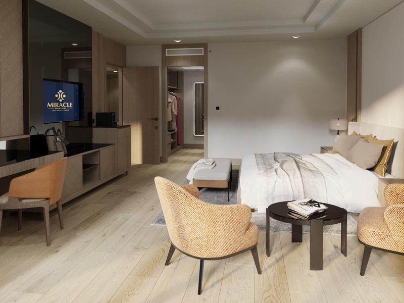 Habitación de hotel moderna con cama, sillas, escritorio y TV en tonos cálidos.