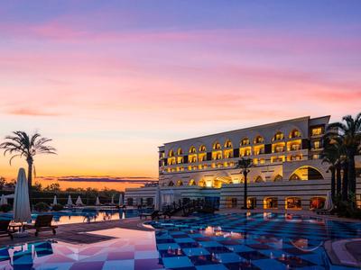 Hotel at sunset with illuminated pool area and palm trees.