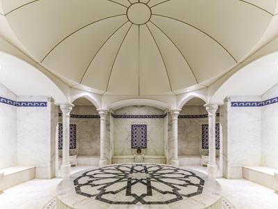 Bright round hammam with vaulted ceiling, marble columns, and a central marble fountain.