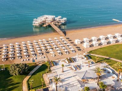 Beach with sun umbrellas, pier, and a restaurant by the sea, surrounded by greenery.