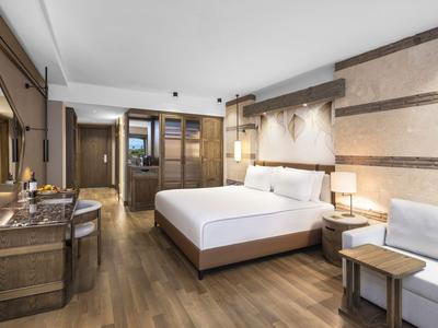 Modern hotel room with double bed, desk, chairs, and wooden floor.