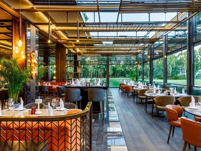 Modern restaurant with glass roof, wooden floor, and elegant tables with leather chairs