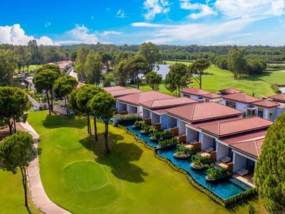 Villas with private pools in a green garden area near a golf course under a blue sky.