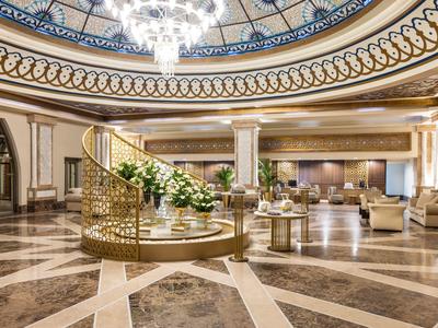 Luxurious hotel lobby with marble floor, central floral arrangement, and ornate chandelier.