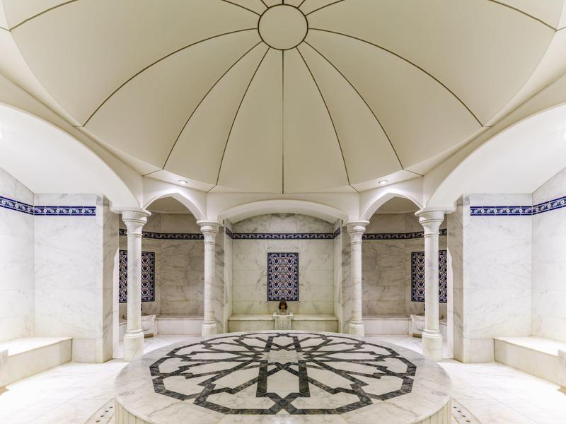Bright round hammam with vaulted ceiling, marble columns, and a central marble fountain.