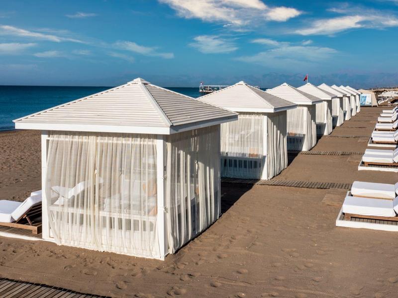 View of beach cabanas and loungers along a sandy beach by the sea under a clear sky.