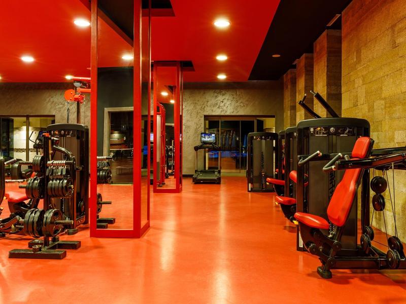A modern gym with red floors, walls, and various exercise equipment.