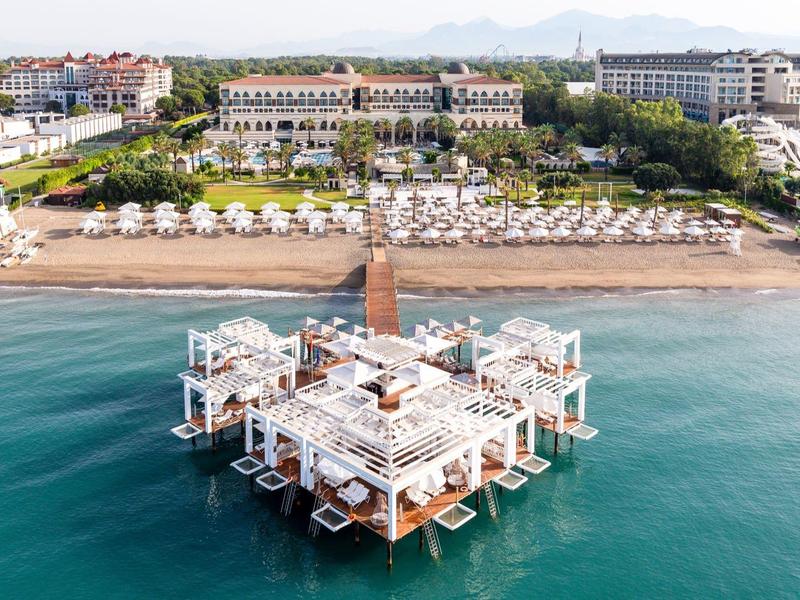 Luxury hotel with overwater restaurant and beach with sun loungers by clear sea.