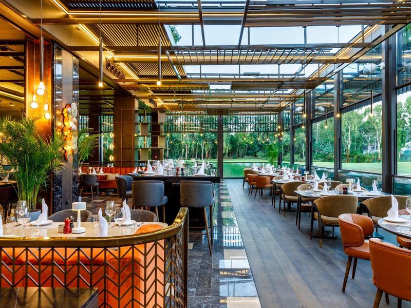 Modern restaurant with glass roof, wooden floor, and elegant tables with leather chairs
