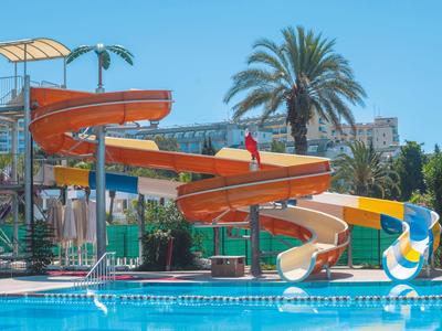 Toboggan aquatique coloré près d'une piscine avec des palmiers et un ciel bleu clair en arrière-plan.