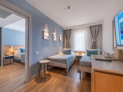 Chambre d'hôtel moderne avec deux lits simples, sol en bois et chambre adjacente.