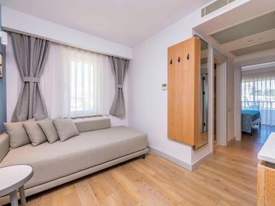 Espace de vie moderne avec canapé clair, rideaux et sol en bois dans une chambre d'hôtel.