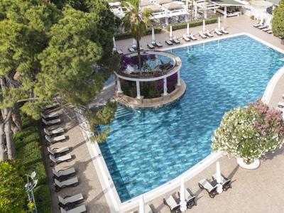 Grande piscine avec des carreaux bleus, entourée de chaises longues et de parasols dans un cadre verdoyant.