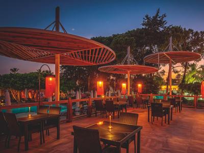 Restaurant en plein air le soir avec des tables éclairées et de grands parasols.