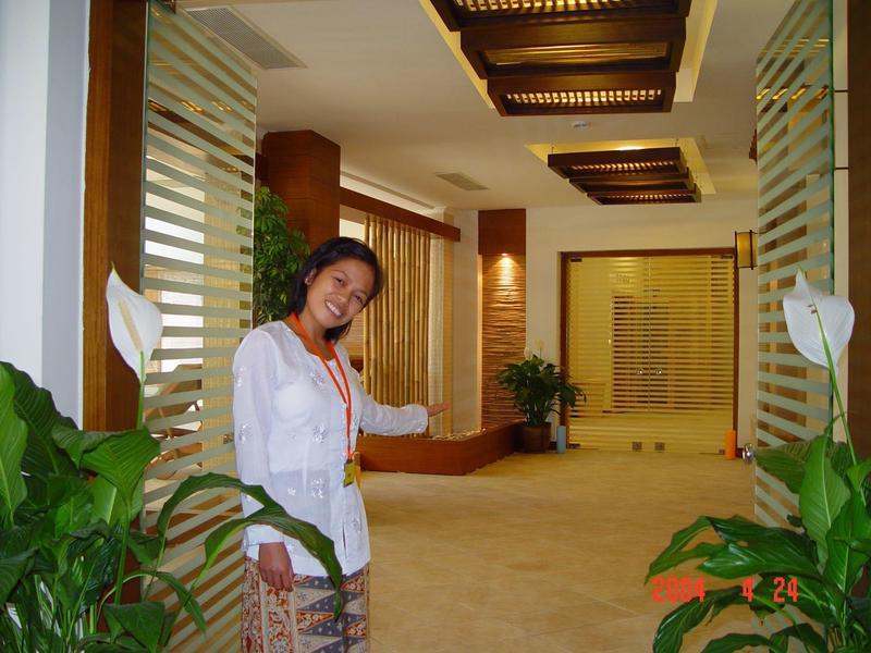 Femme souriante dans un couloir d'hôtel moderne avec des plantes et des accents en bois.