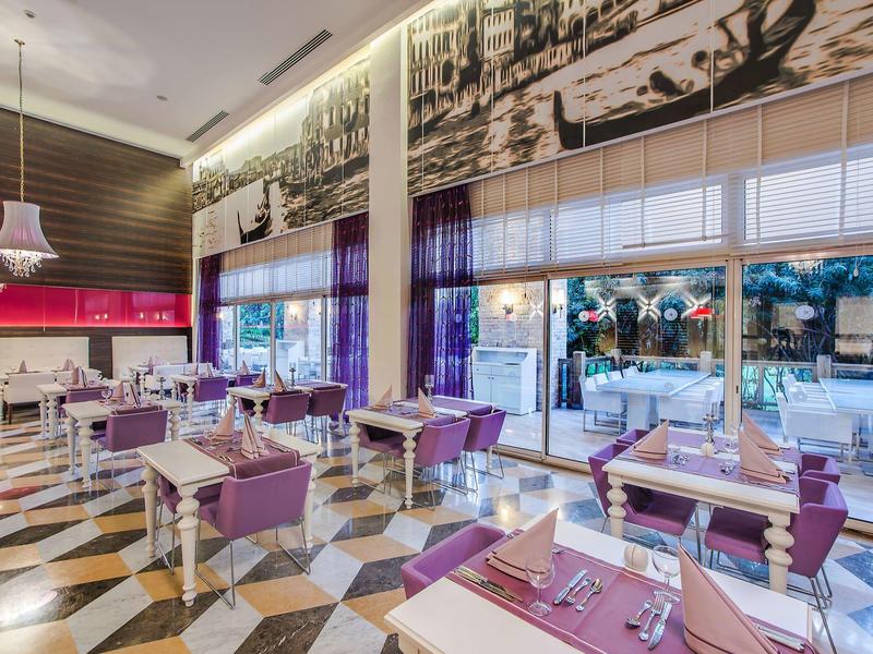 Restaurant moderne avec chaises violettes, tables blanches et une grande fresque au plafond.