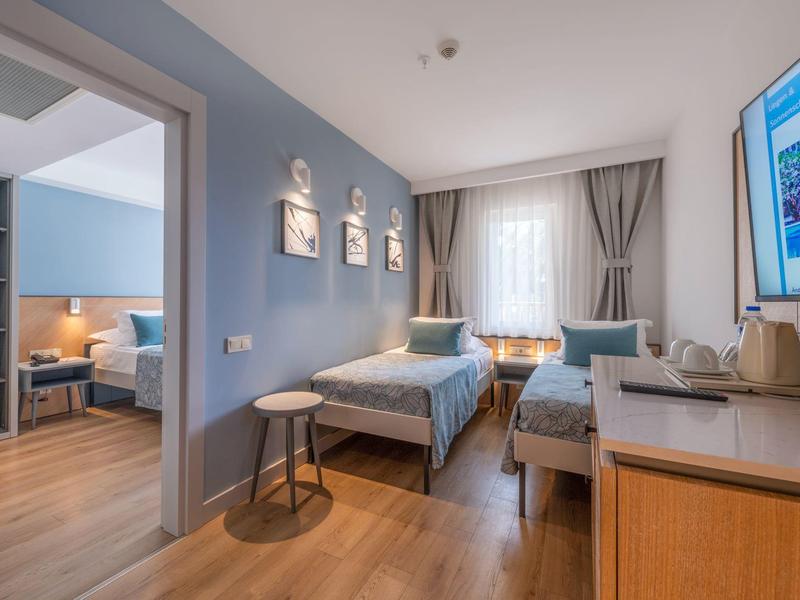 Chambre d'hôtel moderne avec deux lits simples, sol en bois et chambre adjacente.