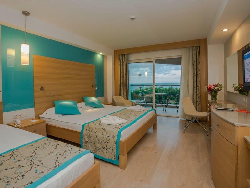 Chambre d'hôtel moderne avec deux lits, bureau et balcon donnant sur la verdure.