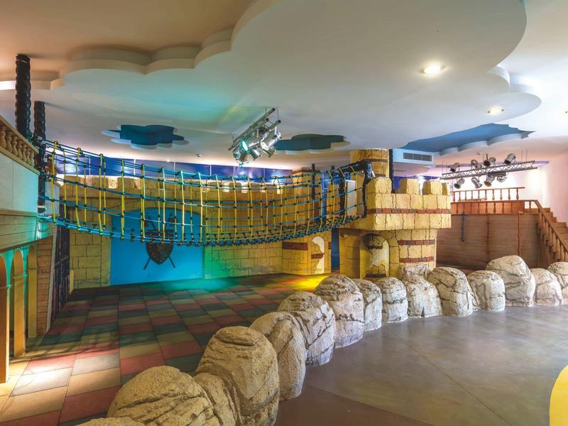 Grand espace intérieur avec poutres en bois, canapés et lumières colorées dans une zone de jeu d'hôtel.