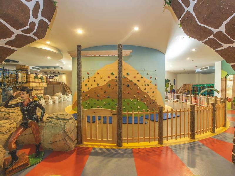 Espace de jeu coloré pour enfants avec motifs de girafe et barrière de sécurité dans un hall d'hôtel.